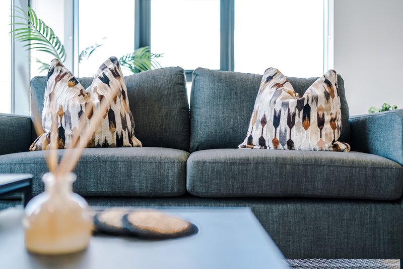 Modern living room with grey sectional sofa, patterned cushions, coffee table and potted plants