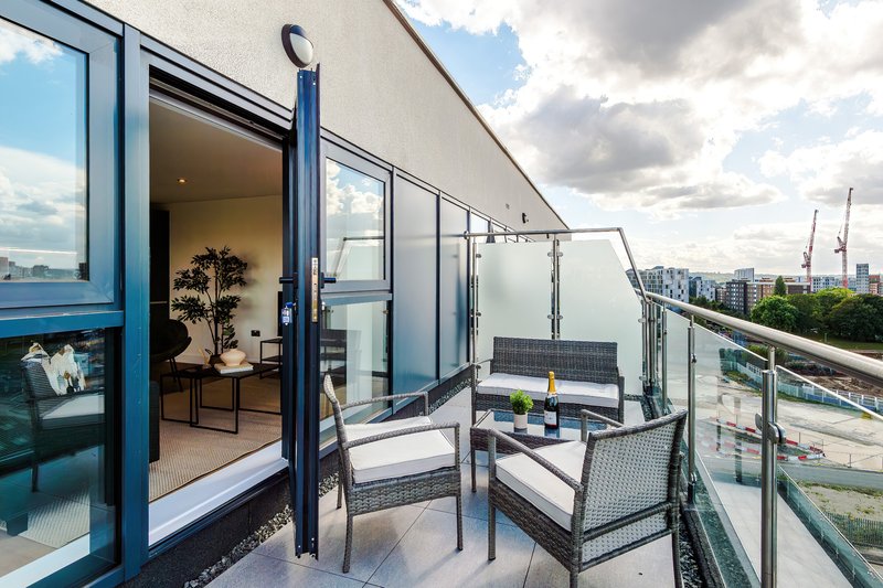 Modern balcony with seating area, glass doors, potted plant and city skyline view