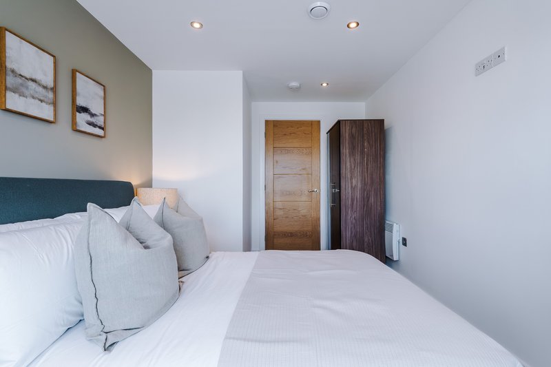 Modern bedroom with double bed, grey headboard, white bedding, framed wall art and wooden doors