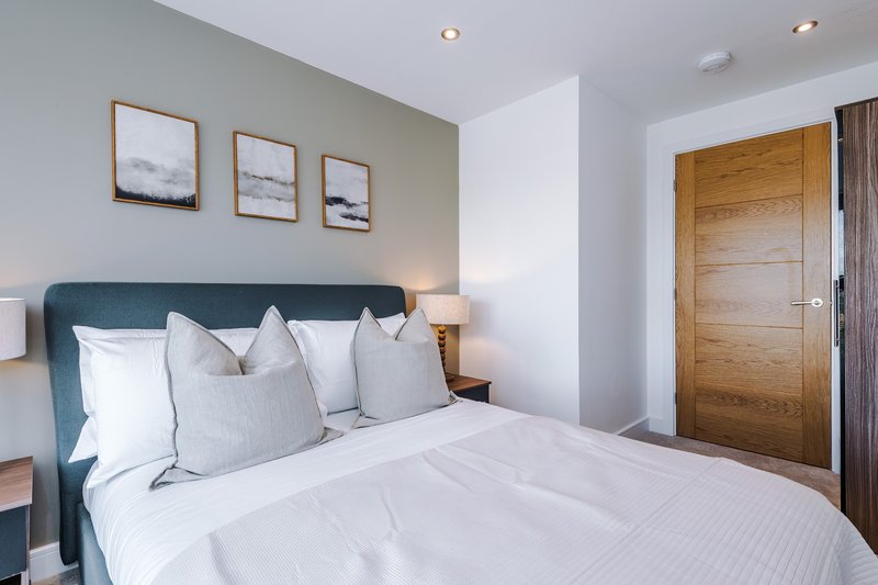 Modern bedroom with teal upholstered bed, white bedding, wooden door and framed wall art
