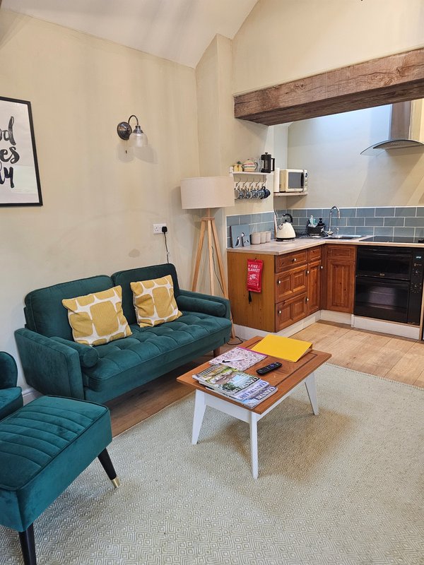 Open-plan living area with teal sofa, kitchen with wooden cabinets, exposed beam ceiling