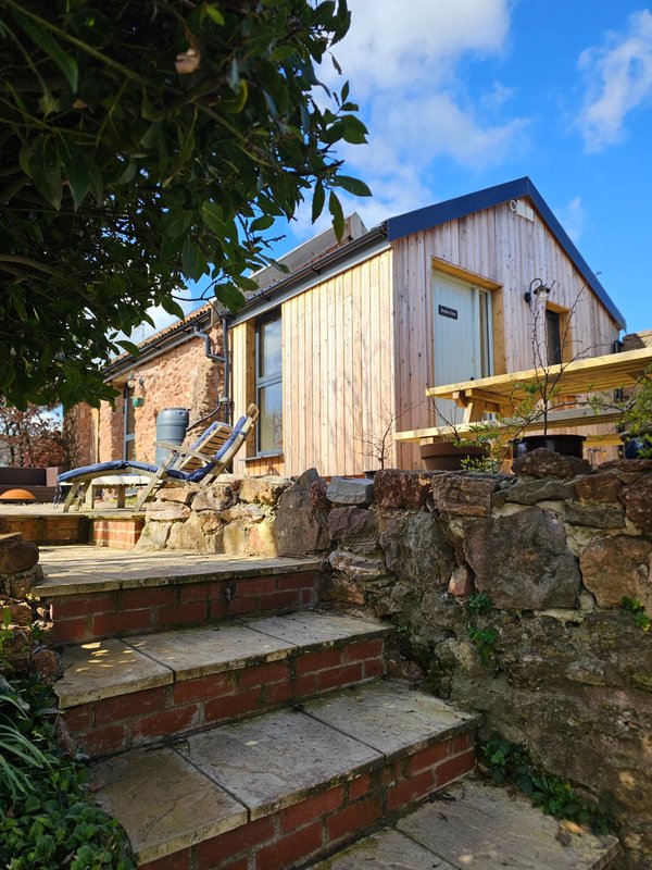 Modern tiny house with wooden cladding, brick steps, stone wall and garden entrance