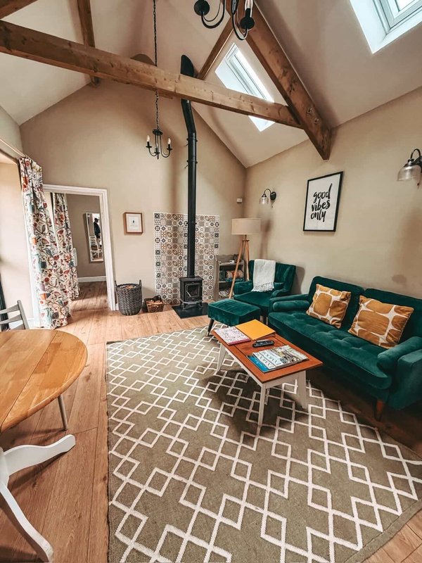 Open-plan living room with exposed wooden beams, green sofa, wood dining table, and geometric patterned rug