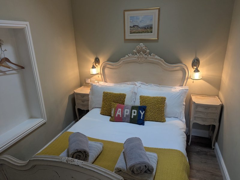 Bedroom with ornate white headboard, double bed, yellow and white bedding, decorative pillows, and bedside lamps