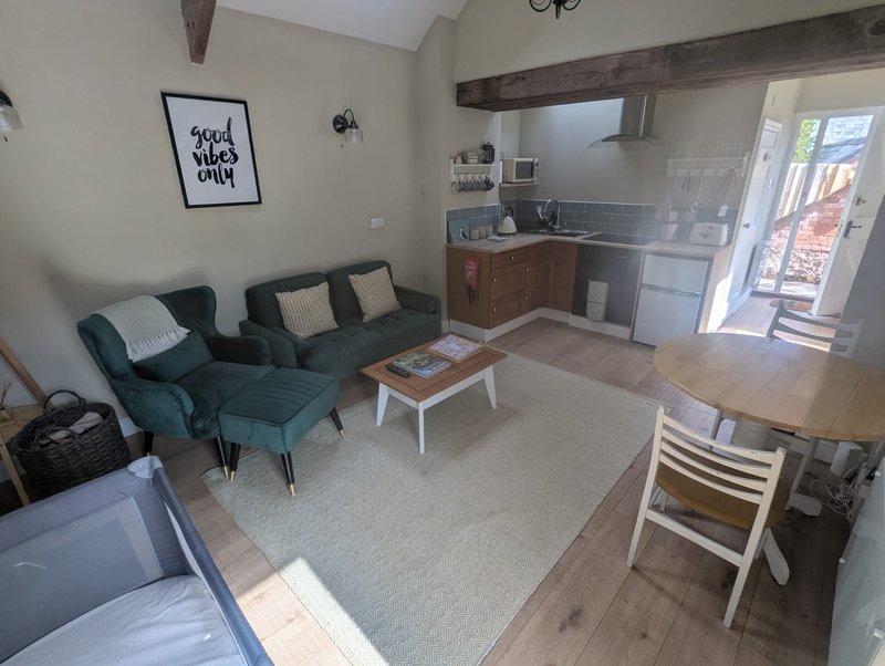 Open-plan living and kitchen area with teal sofa, wooden beams, and dining table
