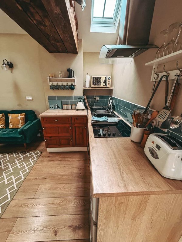 Compact kitchen and bedroom space with wooden flooring, sink, cooker, and green upholstered seating