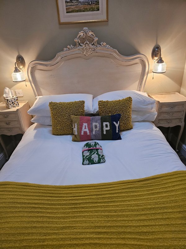 Ornate cream upholstered bed with decorative pillows, bedside lamps, and framed art above