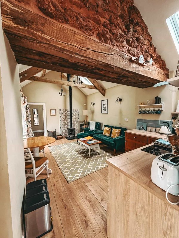Open-plan living space with exposed wooden beam, green sofa, kitchen area and wooden flooring