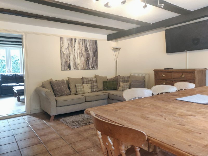 Open-plan living area with sectional sofa, wooden dining table, and exposed beam ceiling