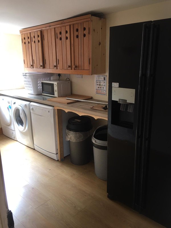 Kitchen with wooden cabinetry, washing machine, microwave, black refrigerator and wooden countertop