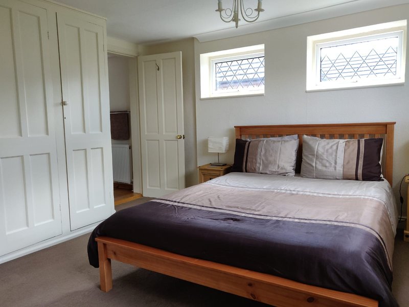 Bedroom with wooden bed, grey bedding, wardrobes, and high windows