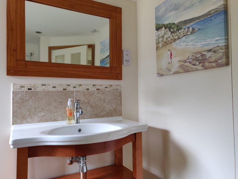 Bathroom with curved white sink, wooden vanity, large mirror, and beach artwork