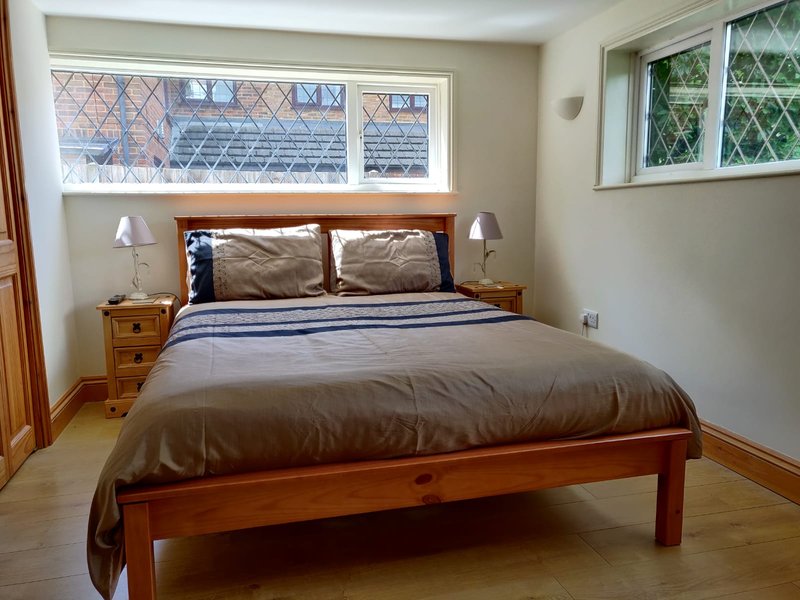 Bedroom with wooden bed frame, brown bedding, side tables with lamps and windows