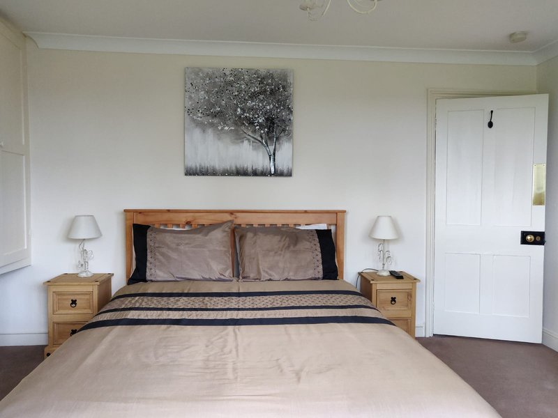 Bedroom with wooden bed frame, grey bedding, bedside tables with lamps, and tree artwork