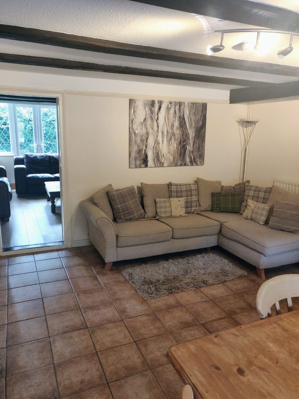 Living room with beige corner sofa, patterned cushions, abstract wall art, and terracotta tile flooring