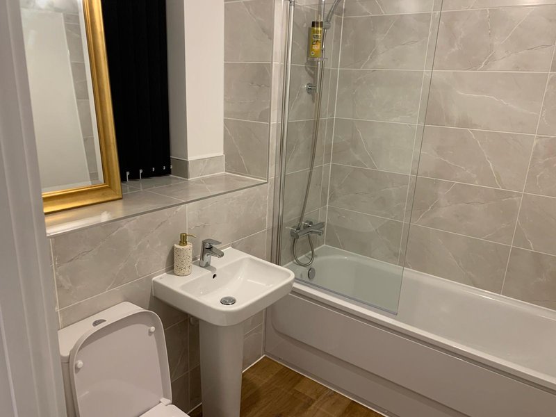 Modern bathroom with white sink, bathtub, shower enclosure, tiled walls and mirror