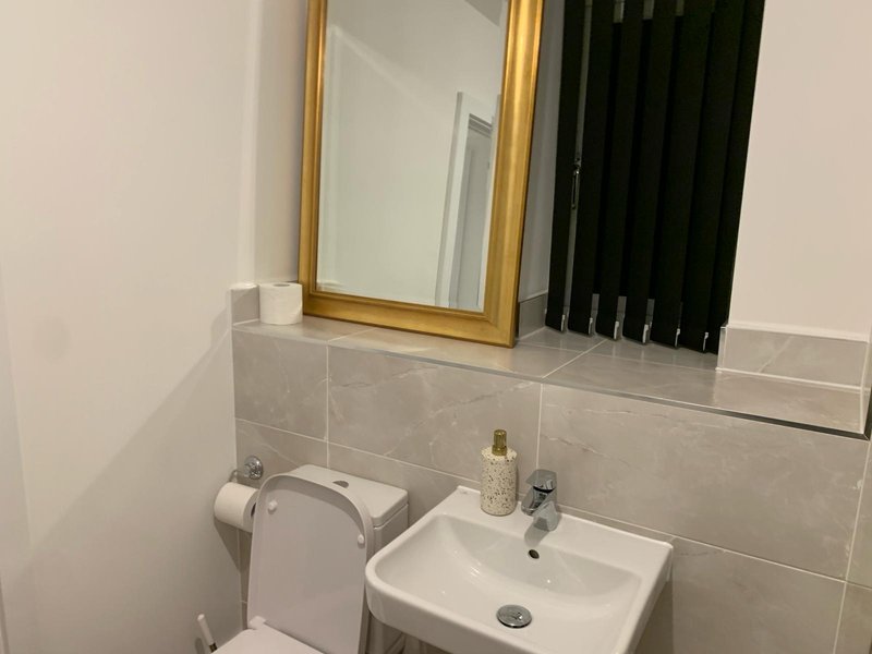 Bathroom with white sink, gold-framed mirror, toilet and tiled walls