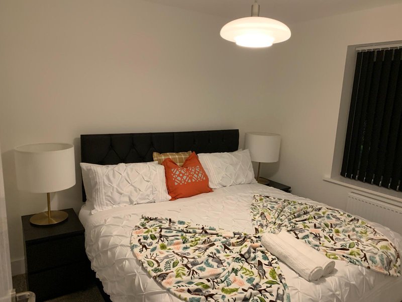 Bedroom with double bed, black headboard, white bedding, decorative pillows and pendant light