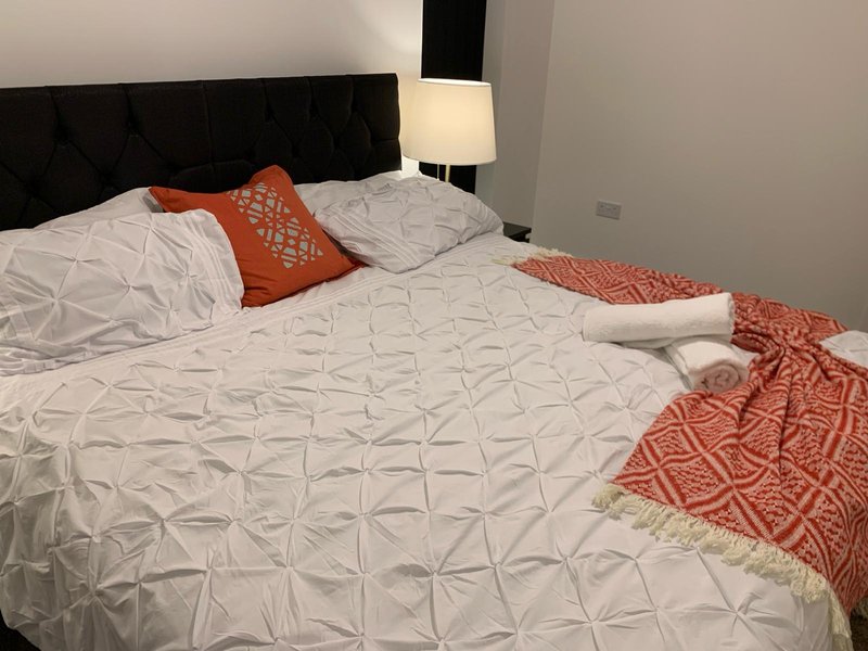 Modern bedroom with double bed, black headboard, white bedding, orange cushions and throws