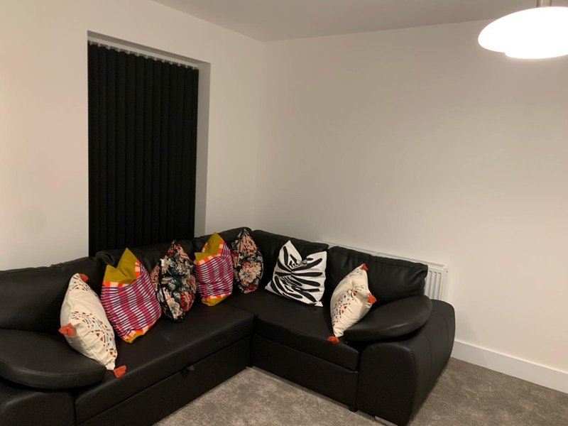 Modern living room with black corner sofa, decorative cushions, dark curtains and ceiling light