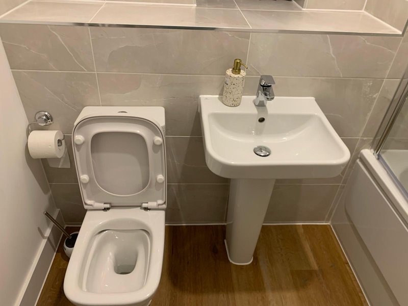 Modern bathroom with toilet, pedestal sink, tiled walls and wooden flooring