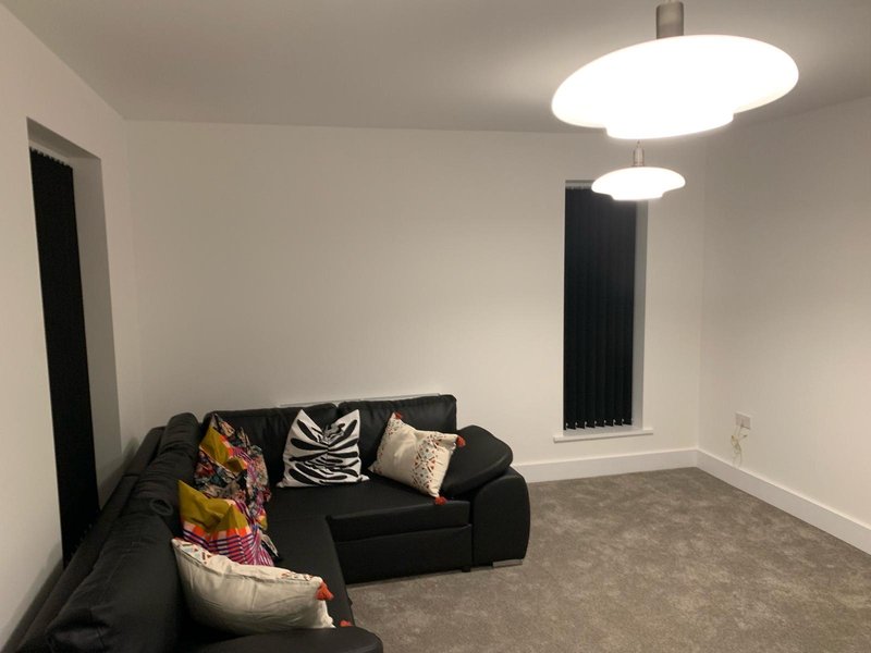 Modern living room with black sofa, decorative cushions, round ceiling lights and grey carpet