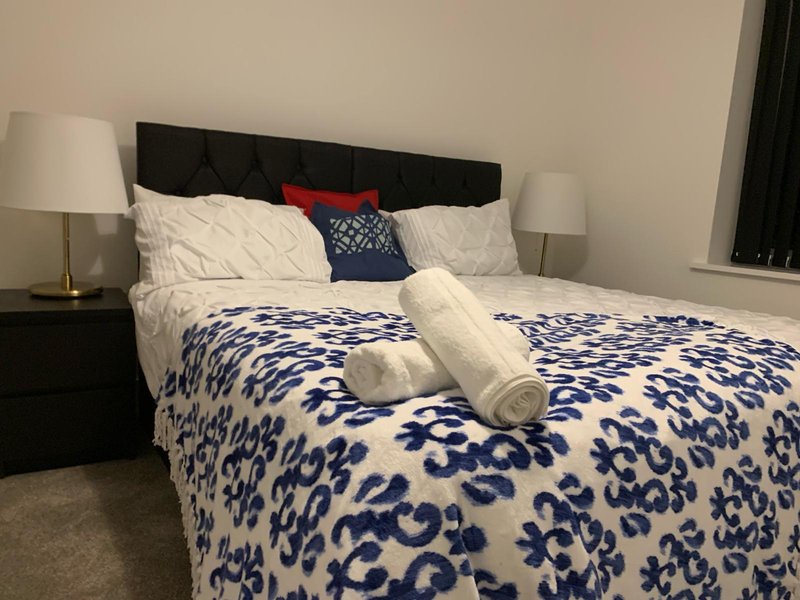 Modern bedroom with black headboard, blue patterned duvet, white pillows and bedside lamps