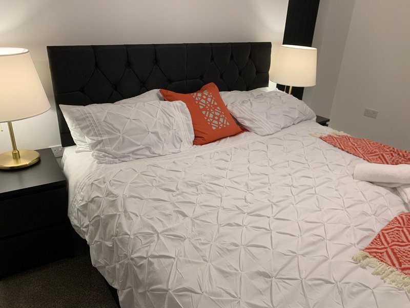 Modern bedroom with black upholstered headboard, white quilted bedding, and orange accent pillows
