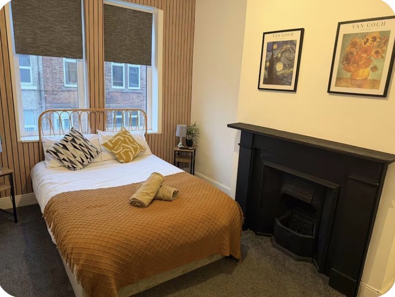 Bedroom with double bed, gold bedspread, decorative pillows, fireplace and framed wall art