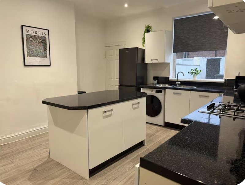 Modern kitchen with white cabinetry, black countertops, island, gas hob and appliances
