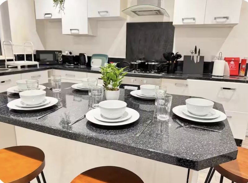 Modern kitchen with white cabinetry, granite island, place settings and orange bar stools