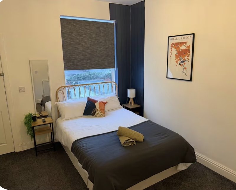Modern bedroom with double bed, bedside table, window with blue blind, and wall art