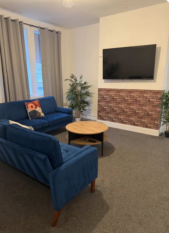 Modern living room with blue sofa, wooden coffee table, wall-mounted TV and brick fireplace