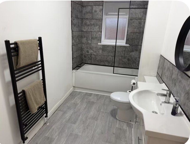 Modern bathroom with white sink, toilet, black heated towel rail, and shower enclosure