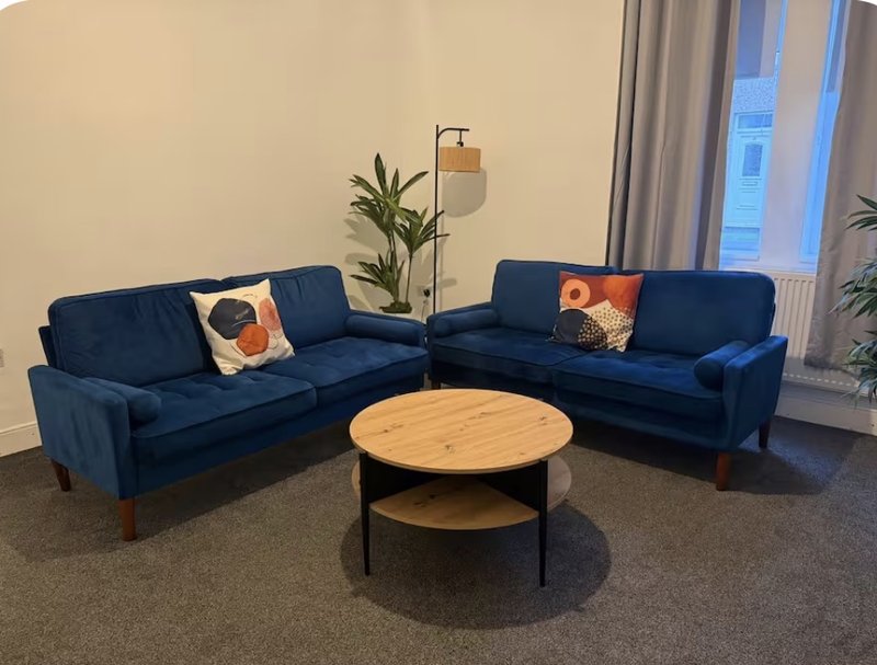 Modern living room with blue corner sofa, round wooden coffee table, potted plants and floor lamp