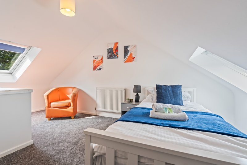 Attic bedroom with double bed, orange armchair, blue bedding and framed wall art