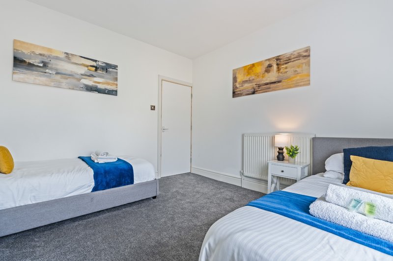 Bright bedroom with two single beds, grey carpet, white walls and modern decor