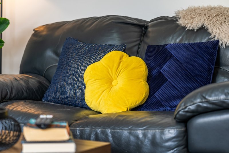 Black leather sofa with blue and yellow decorative cushions and a cream throw