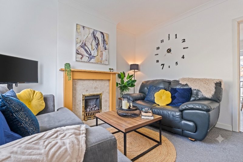 Bright living room with fireplace, grey sofa, blue leather armchair, wooden coffee table and wall clock