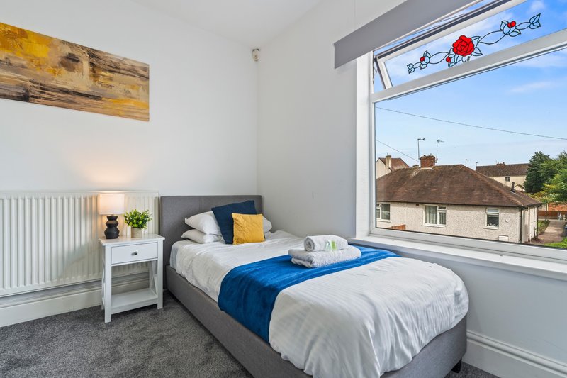 Modern bedroom with single bed, blue bedding, white nightstand, and large window with countryside view