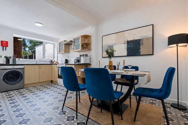 Open-plan kitchen and dining area with blue chairs, wooden cabinetry, and patterned flooring