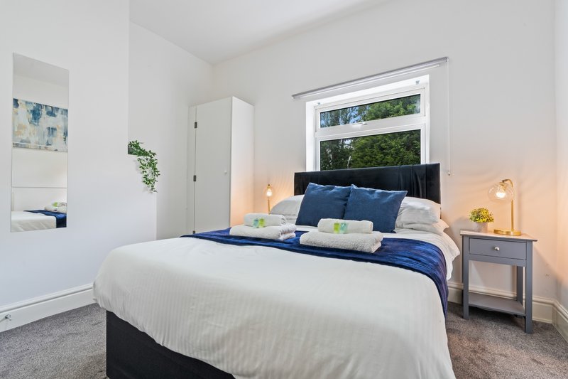 Bright bedroom with double bed, blue bedding, bedside lamps and large window