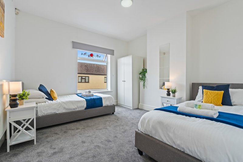 Bright twin bedroom with two beds, white furniture, grey carpet and window view