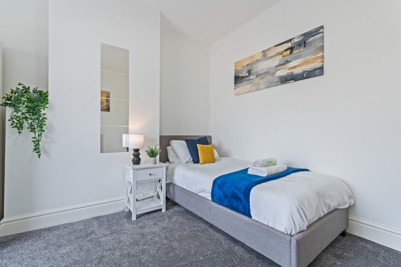 Modern bedroom with double bed, blue throw, white bedside table, mirror and hanging plant