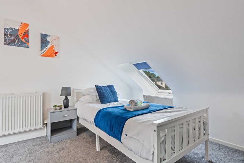 Bright bedroom with single bed, white wooden frame, blue bedding, and wall art