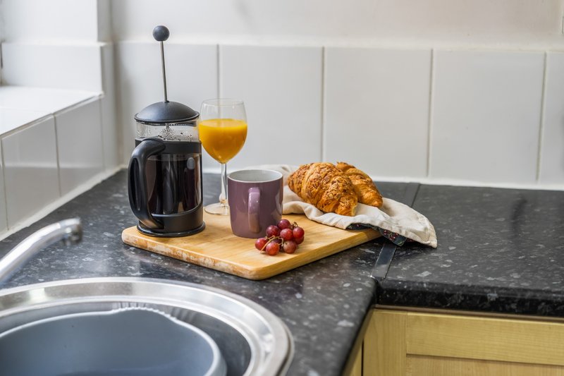 Kitchen counter with coffee maker, orange juice, croissant and fresh berries on wooden board