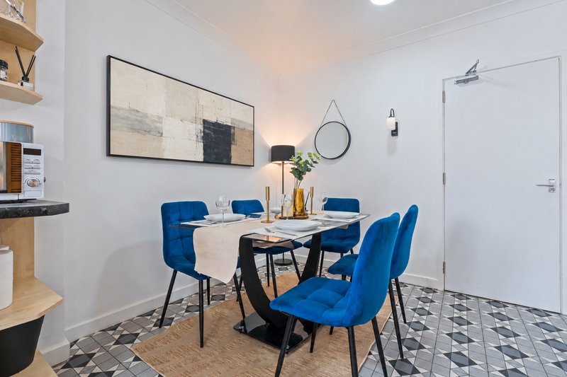 Modern dining area with blue chairs, black table, framed artwork and potted plant
