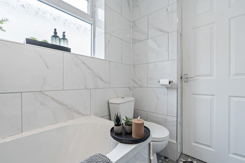 Modern bathroom with white marble tiles, bathtub, toilet, and decorative accessories on shelf