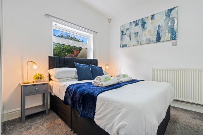 Bright bedroom with double bed, blue bedding, dark headboard, and bedside lamp