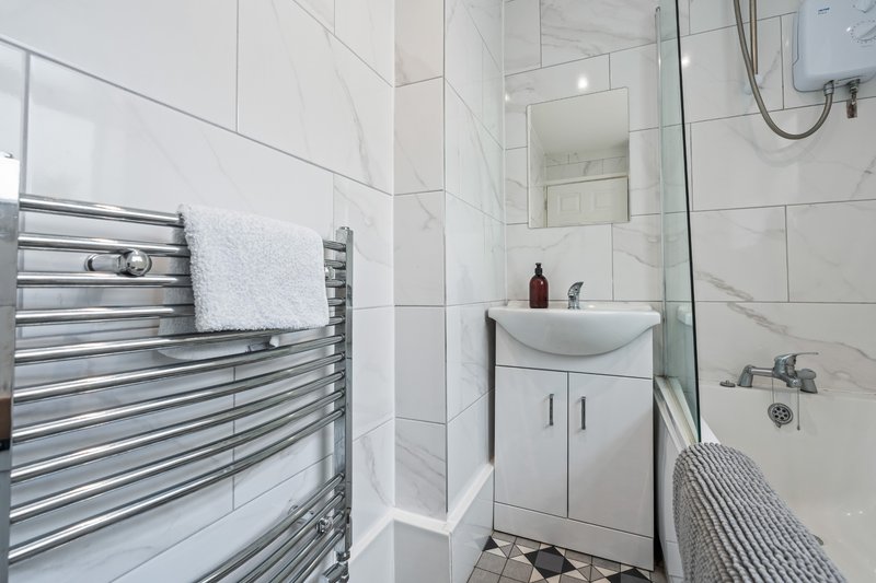 Modern bathroom with white tiles, chrome heated towel rail, white sink vanity and shower enclosure